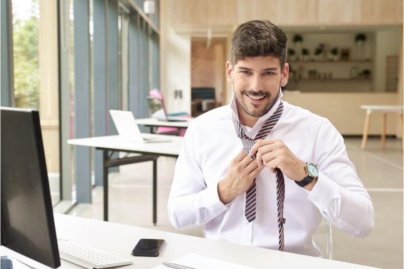 man tying tie while sitting at office