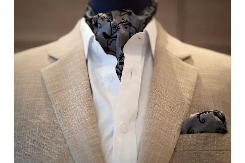 Close up of beige jacket suit with white shirt and ascot tie scarf